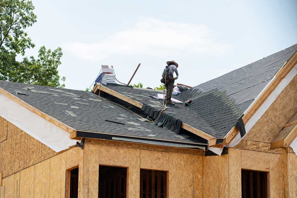 A homeowner examines a stained ceiling below a damp attic with exposed insulation and roof framing.