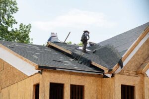 A homeowner examines a stained ceiling below a damp attic with exposed insulation and roof framing.